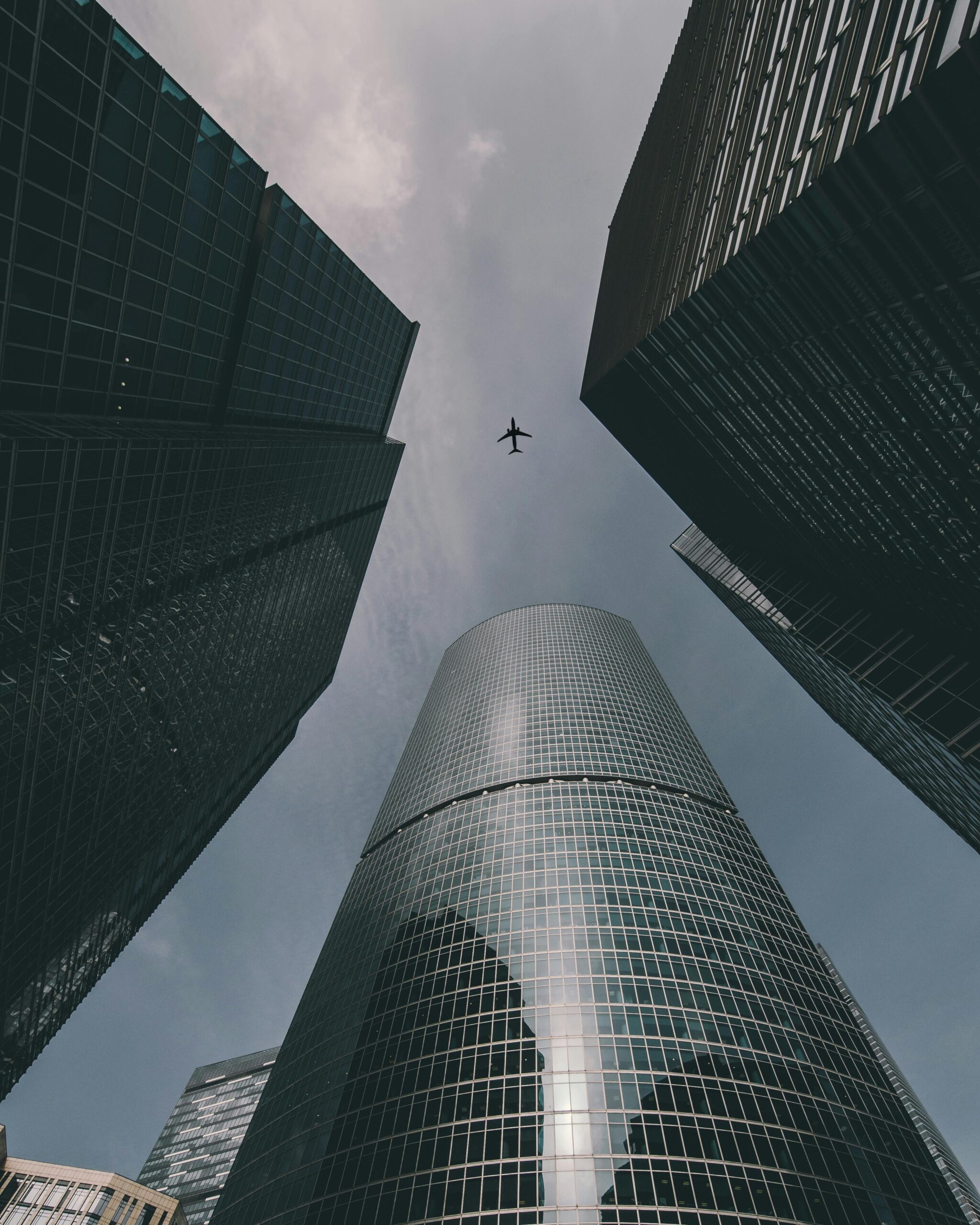 Low angle shot of skyscrapers framing an airplane flying overhead. Captures urban modernity.