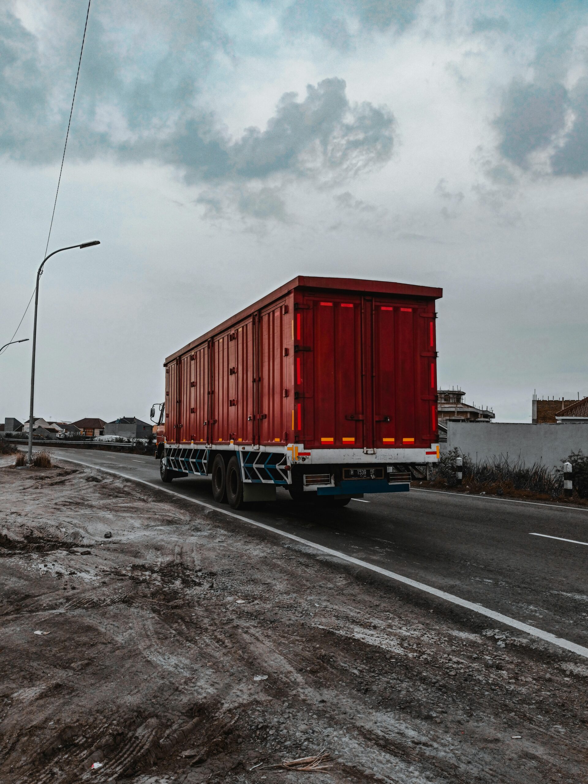 Large heavy motor vehicle driving on roadway while transporting goods along village in cloudy day
