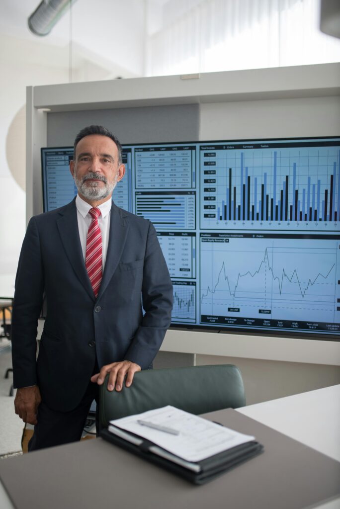Confident businessman in office with data charts, analysis, and growth graphs on screen.